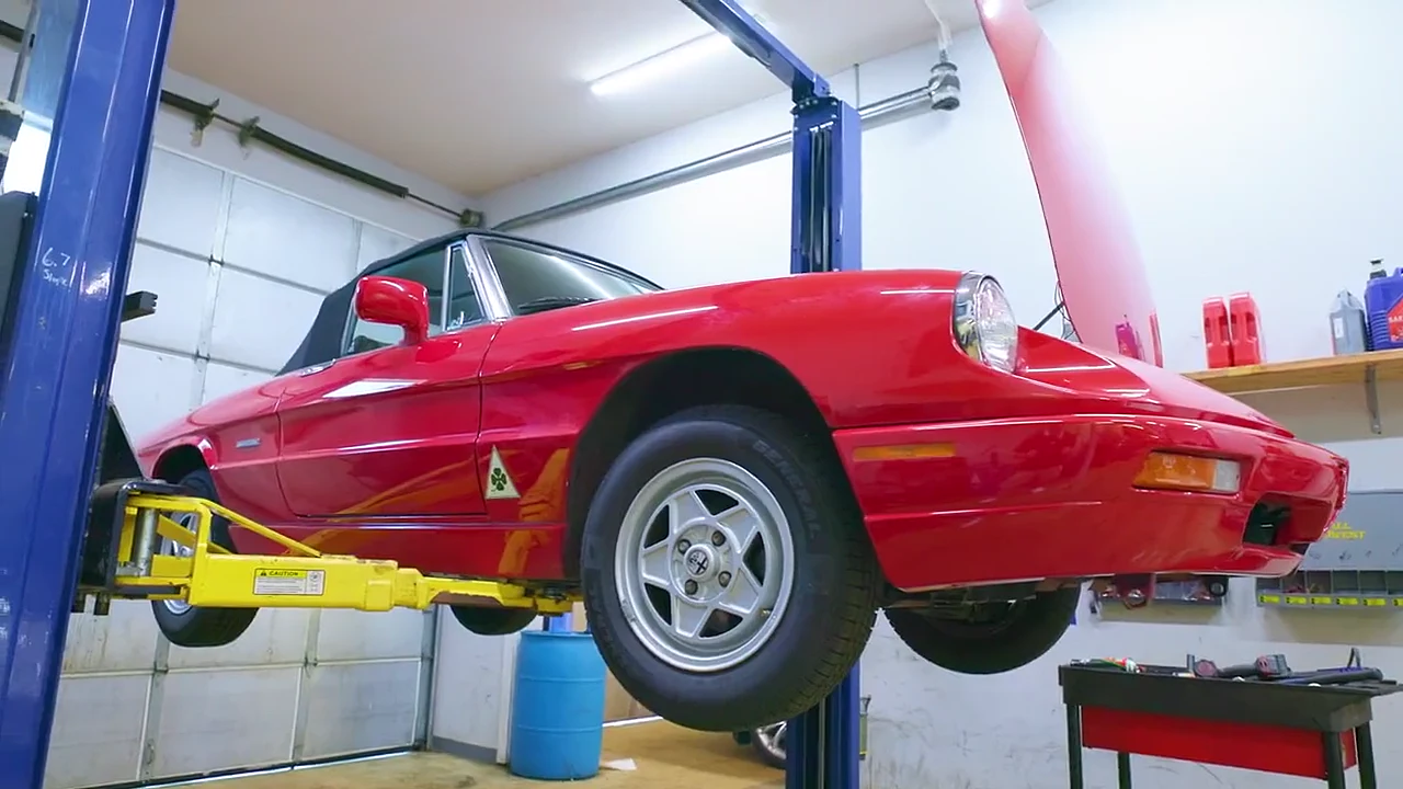 A red Alfa Romeo Spider on the lift with its wheels hanging