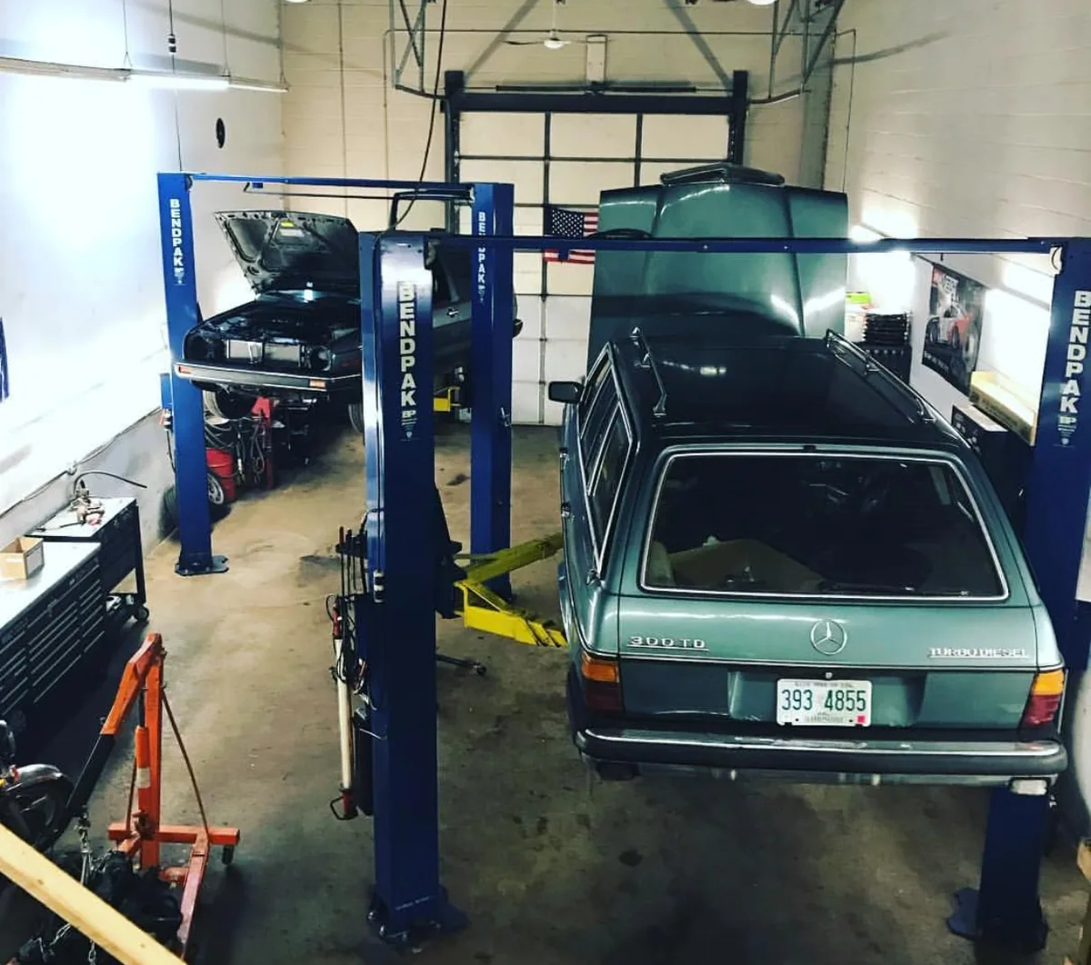 A green Mercedes-Benz W123 wagon in the shop between two lifts